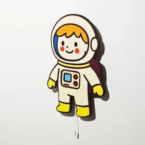 Astronot lambanın yandan görünümü, ışığı kapalı; krem rengi kıyafet, bordo sırt çantası ve duvardaki gölgesi