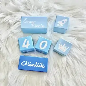 Mavi tonları anı küpü seti beyaz tüylü örtüde; açık mavi isim bloğu, mavi rakam küpleri ve Günlük yazılı mavi blok