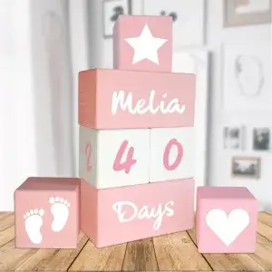 Pembe-Beyaz-Pembe anı küpü seti ahşap masada; yıldız, ayak izi ve kalp simge küpleriyle üst üste dizili bloklar