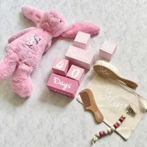 Pembe tonları anı küpü seti pembe peluş tavşan, isimli ahşap fırça ve tarakla birlikte keten kese üzerinde