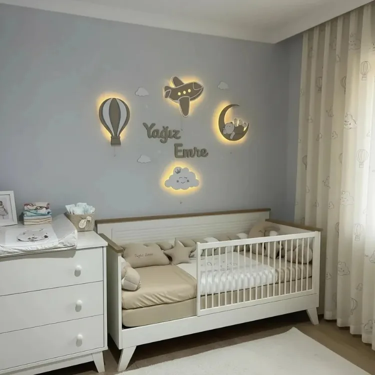 Işıklı uçan balon, uçak, bebek ayılı ay ve gülen bulut lamba, ortada ışıksız ahşap isim, beşikli odada