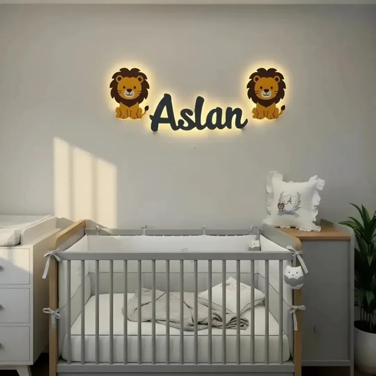 İki aslan ahşap lamba ve ışıklı isim lamba, gri duvarda beyaz beşiğin üstünde örnek isimle