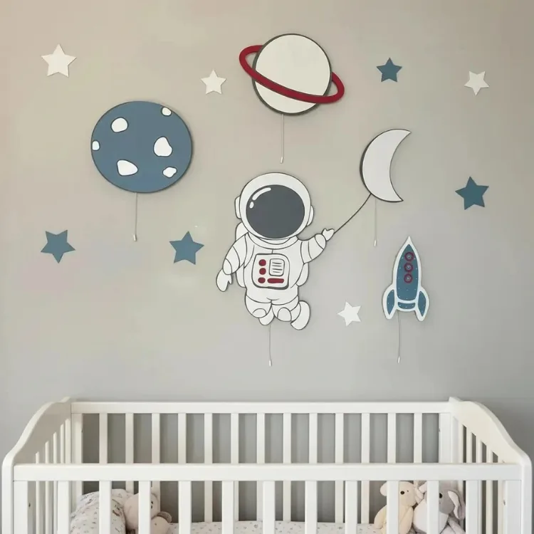 Astronot, satürn, ay, roket ve mavi gezegen ahşap lambaları, yıldızlı duvarda beyaz beşiğin üstünde
